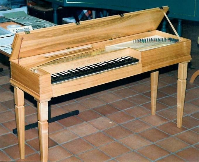 Clavichord aus hellem Holz mit aufgeklapptem Deckel, schlichtes rechteckiges Gehäuse auf gedrechselten Beinen.